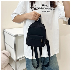 Detail of a black mini nylon backpack showing front zipper pocket and side woven label tag
