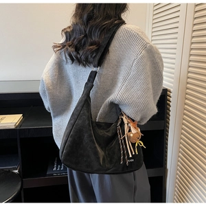 Détail du sac hobo en daim noir avec lettrage blanc et breloque ours sur l'épaule