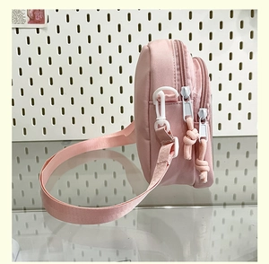 Detailed side view of pink nylon crossbody bag with dual-zipper structure and woven strap