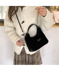 Close-up of black faux fur handbag featuring leather handles and gold metal logo detail