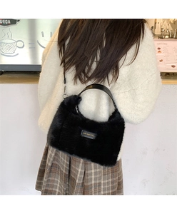Detail of a black plush crossbody bag with leather handle and love every day tag on a model