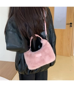 Pink plush shoulder bag with leather strap and tag shown in a lifestyle setting