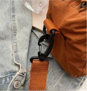Detail showing the black swivel carabiner and thick nylon shoulder strap of a brown bag