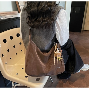 Détail du sac cabas en daim marron avec pendentif ours et logo sur la bandoulière