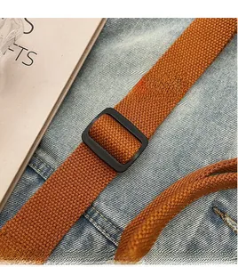 Detail of adjustable caramel woven shoulder strap with black matte buckle on denim background