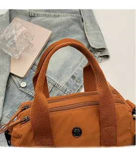 Close-up of caramel brown nylon tote bag with three zipper compartments on denim jacket
