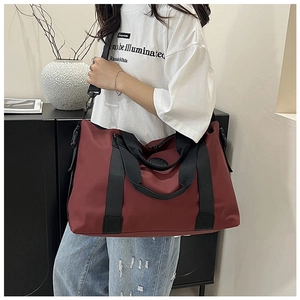Burgundy travel bag worn by a model in a modern home setting showing shoulder strap detail