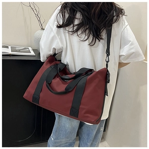 Detail view of burgundy travel bag with black straps being carried by a model