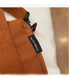 Detail of caramel nylon shoulder bag featuring woven brand label and black metal hardware