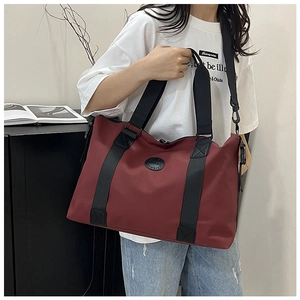 Detailed view of burgundy travel tote bag with wide black shoulder straps and round logo