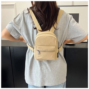 Detail view of khaki mini nylon backpack showing side brand label and front zipper pocket