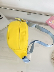 Detail der gelben Crossbody-Brusttasche mit blauem Gurt und Fashion-Label auf dem Tisch