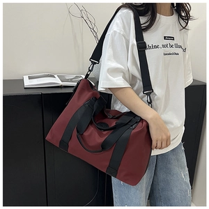 Close-up of wine red travel duffel bag with black straps and metallic buckles on model