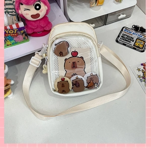 Detail of cream canvas crossbody bag featuring clear PVC window with five capybara badges