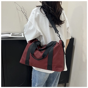 Rear view of model carrying a large burgundy travel bag with black adjustable strap