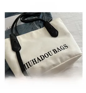 Détail du sac cabas en toile blanche avec bandoulières en cuir noir et logo