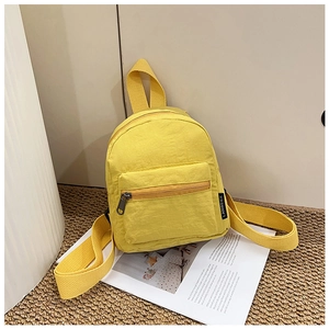 Close-up of a mini yellow nylon backpack with front zipper pocket on a magazine background