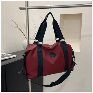 Detailed view of burgundy nylon travel bag with black handles on a minimalist shelf display