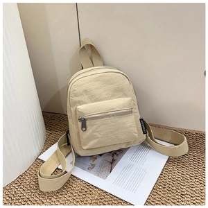 Close-up of beige nylon mini backpack featuring the front zipper pocket and fabric texture