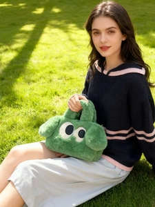 Détail du sac à main peluche vert motif chien avec de grands yeux sur l'herbe