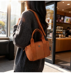 Detail of orange nylon shoulder bag with adjustable wide strap in a cozy cafe setting