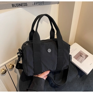 Black nylon Boston bag with round metal logo and adjustable shoulder strap detail
