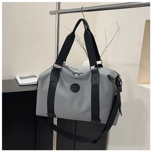 Detail view of large gray travel bag with black straps and round brand logo on metal rack