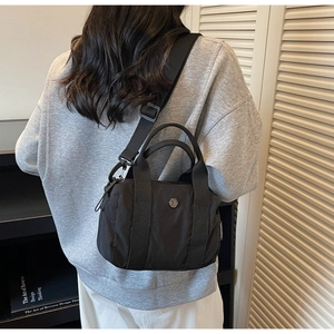Close-up of black nylon crossbody bag featuring round metal logo and woven side tag