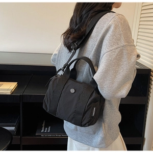 Detailed side view of a black nylon barrel bag featuring a durable woven strap and logo badge