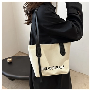 Détail d'un sac cabas en toile blanc cassé avec anses en cuir noir porté par un mannequin