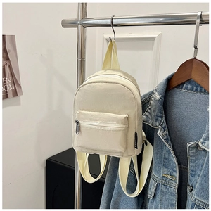 Detail of a creamy white mini nylon backpack with zipper pockets and a side brand tag