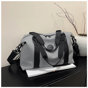 Detail view of grey waterproof travel bag with black straps and metal hooks on a black desk