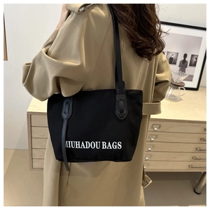 Détail du sac cabas noir en toile avec inscription blanche et bandoulière en cuir
