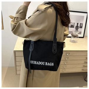 Détail du grand sac cabas noir avec lettrage blanc porté sur un trench-coat chic