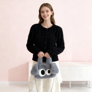 Détail du sac peluche gris avec grands yeux et chaîne dorée porté par un modèle