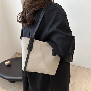 Grand sac fourre-tout en toile beige avec anses en cuir noir porté par un mannequin en studio