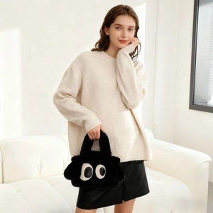 Détail d'un sac à main en peluche noire avec motif grands yeux porté par un mannequin chic