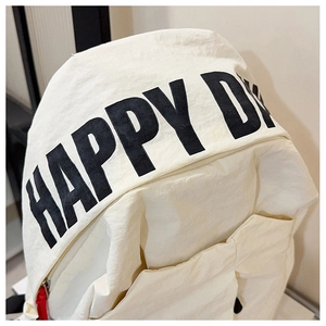 Detailed view of the Happy Day text print and textured nylon fabric on the white backpack