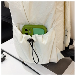 Detail showing the side drawstring pocket of a cream nylon backpack with a mobile phone