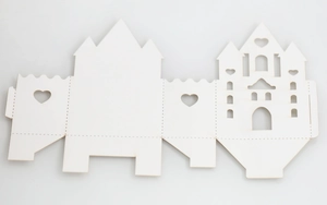 Flat lay view of a laser-cut white castle paper wedding favor box with heart hollow designs