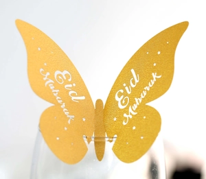 Macro shot of gold butterfly place card with Eid Mubarak text on glass rim