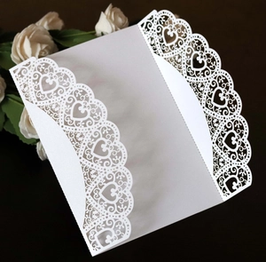 Detail of white laser-cut wedding invitation with heart lace pattern and shimmer finish