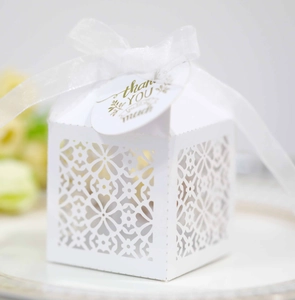 Detail of laser-cut floral wedding favor box with white ribbon and thank you tag