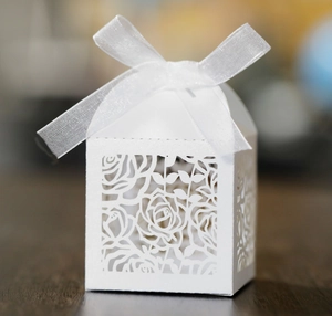 Elegant white laser-cut hollow rose candy box with a white ribbon bow for weddings