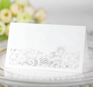 Laser-cut white floral lace place card on a gold-rimmed plate for wedding table decor