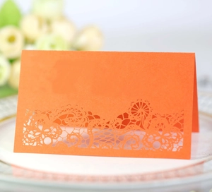 Macro shot of laser-cut orange wedding place card with intricate floral lace patterns