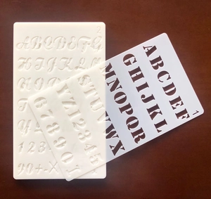 Detail of laser-cut transparent PET stencils with cursive letters and serif numbers
