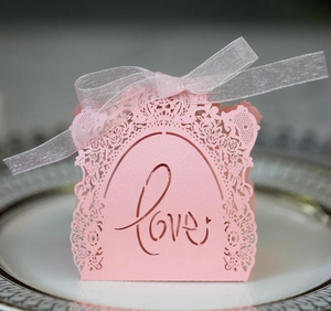 Pink laser cut Love wedding favor box with rose patterns and silver ribbon on a plate
