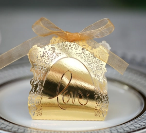 Golden laser-cut wedding favor box with LOVE pattern and organza bow on white plate