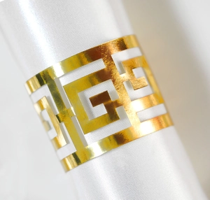 Elegant gold reflective napkin ring with geometric hollow pattern on white fabric